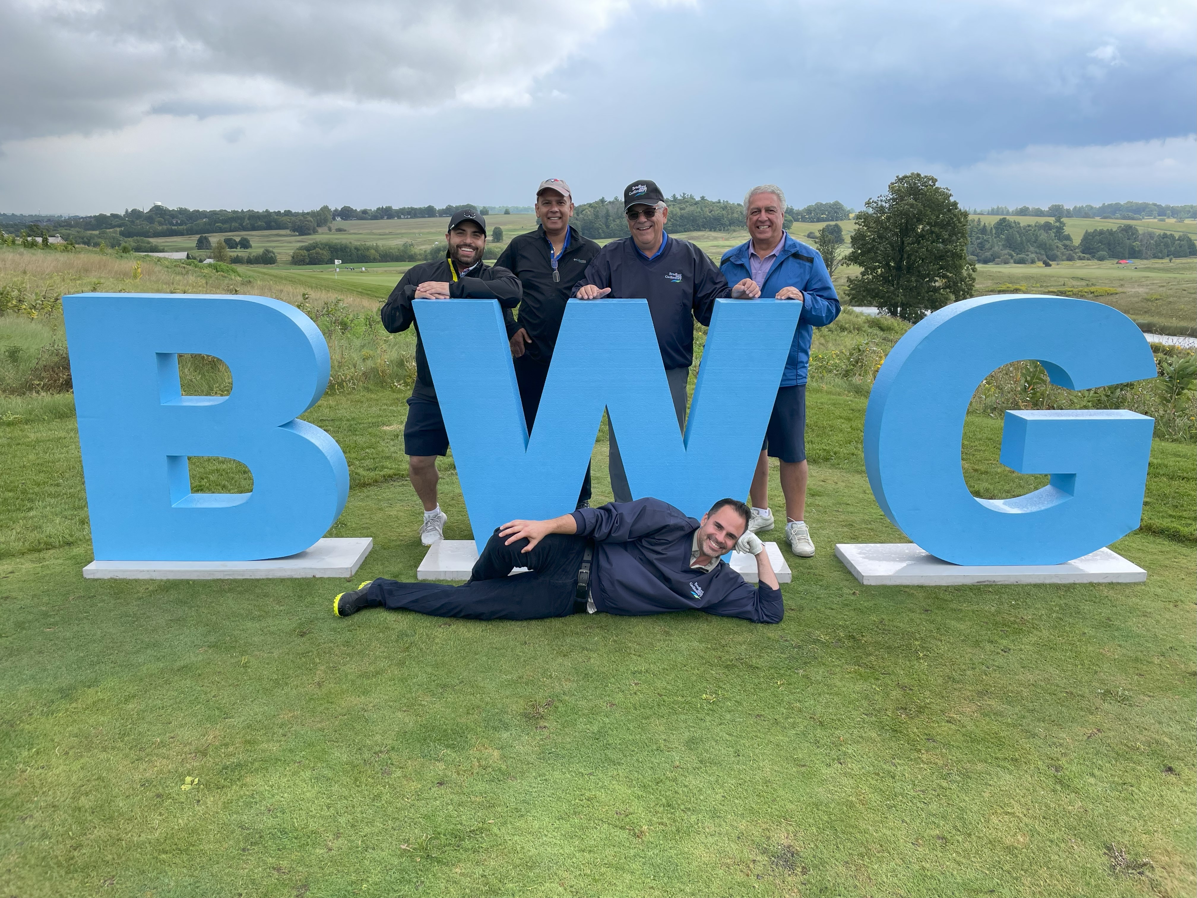 Mayor's Golf Group of golfers standing on a golf hole behind larger BWG letters.