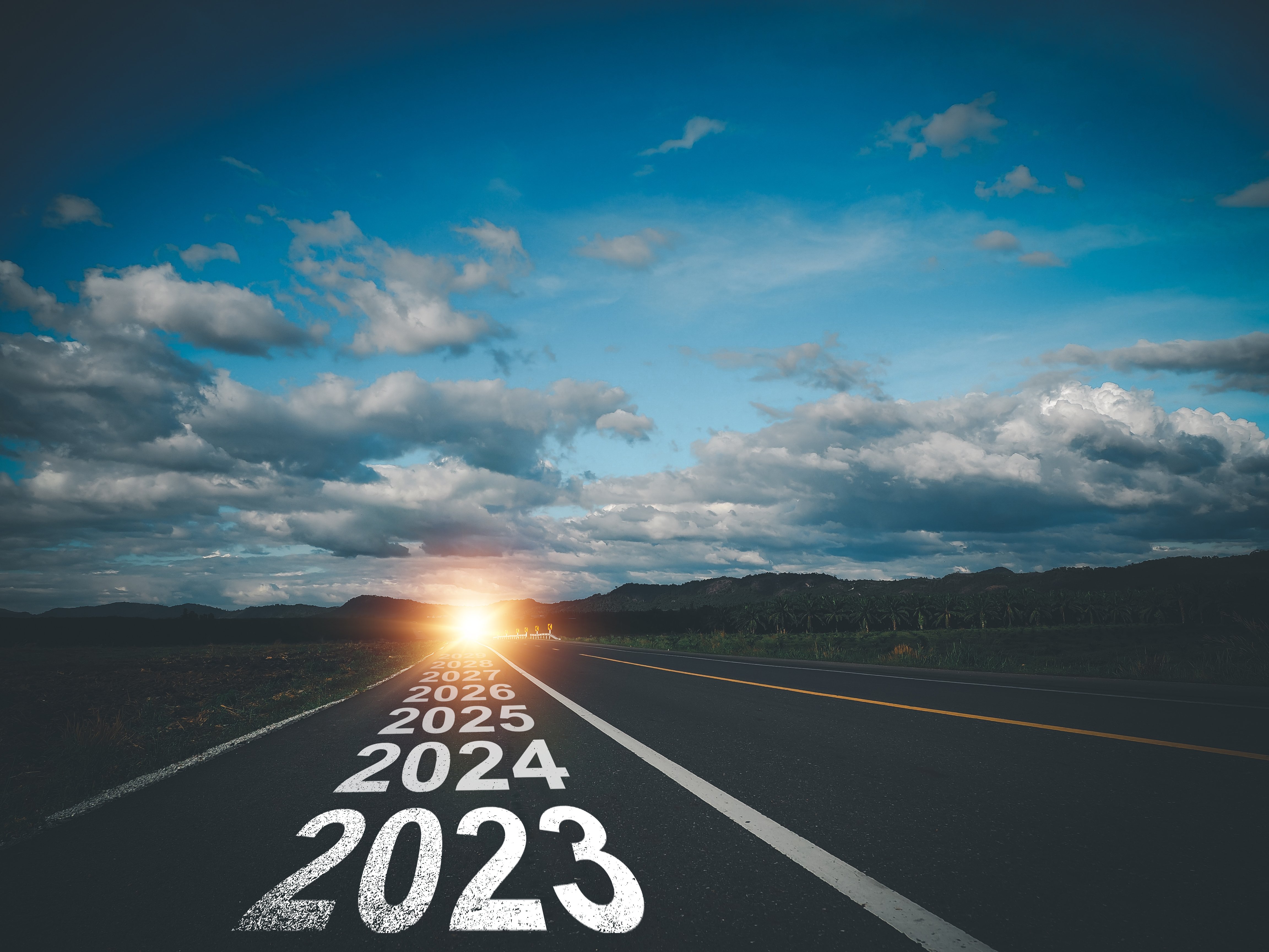 Photo of roadway with the years 2023, 2024 continuing with a blue cloudy sky