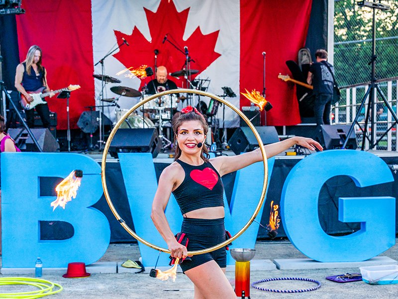 Image of flame performer in front of BWG sign and Canada Day stage with flame hoop